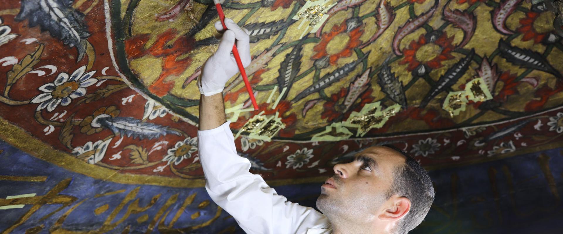 رئيس فريق الترميم مختار عبد العزيز يعمل على طلاء الخشب داخل ضريح الإمام محمد الشافعي في القاهرة. (Courtesy of Megawra)