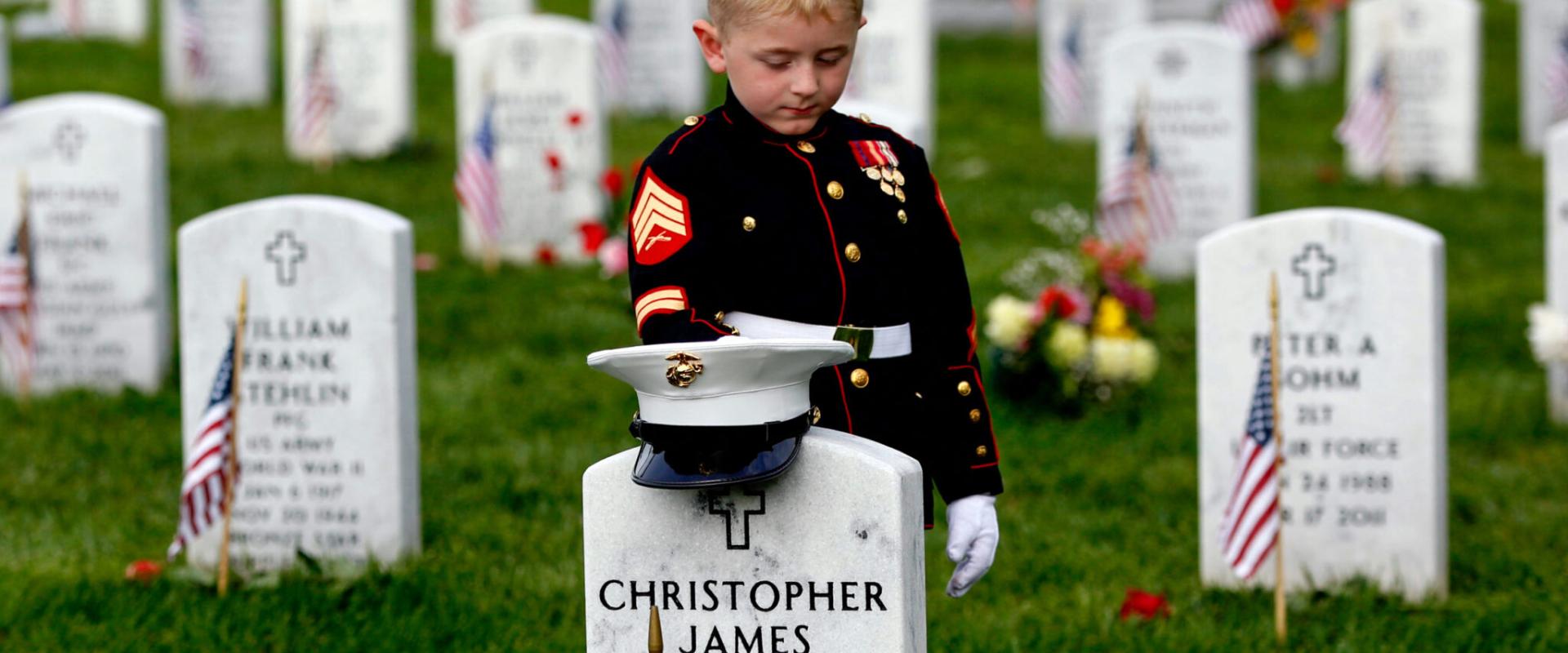 كريستيان جاكوب، 5 سنوات، من هتفورد بولاية نورث كارولينا، يرتدي زي البحرية الأميركية، واقف أمام شاهد قبر والده في يوم الذكرى بمدافن أرلينغتون الوطنية. (© Carolyn Kaster/AP Images)